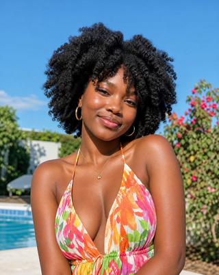 Young Black woman with moisturised 4C curls wearing a colourful summer dress beside a swimming pool.